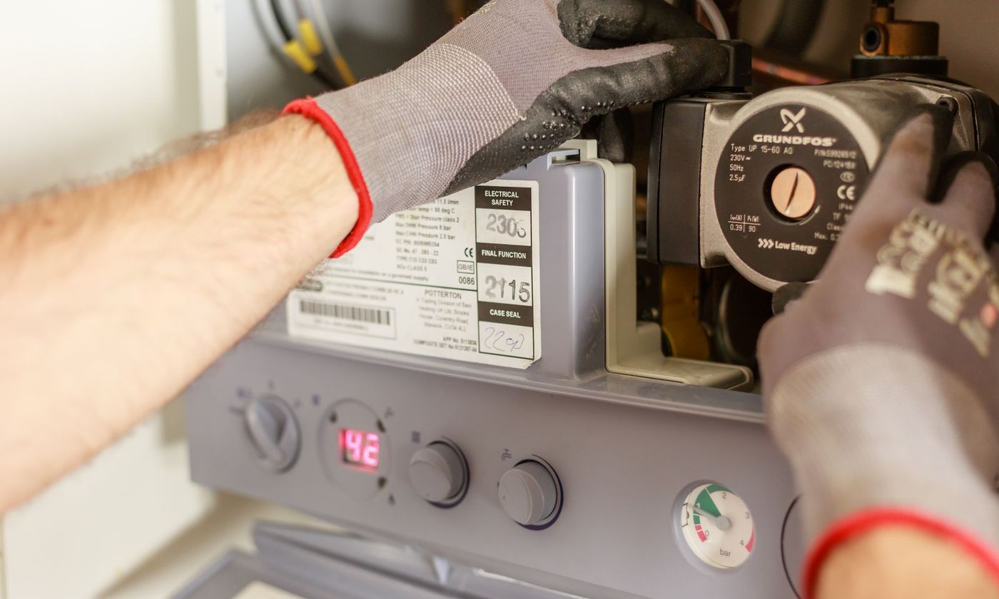 Technician in work gloves adjusting the controls of a wall-mounted gas unit
