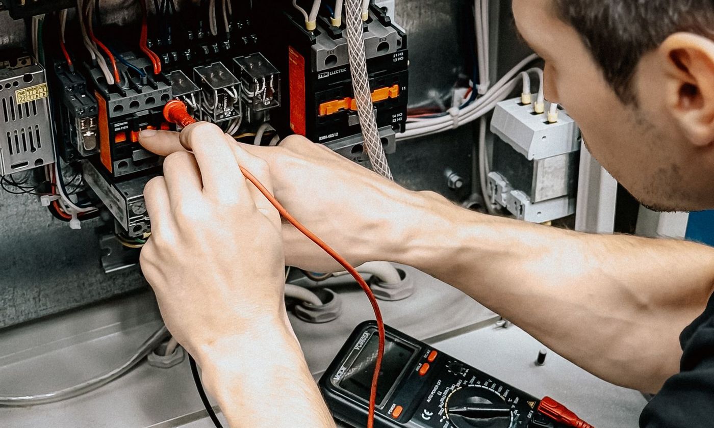 Technician testing thermostat wiring terminals with a multimeter